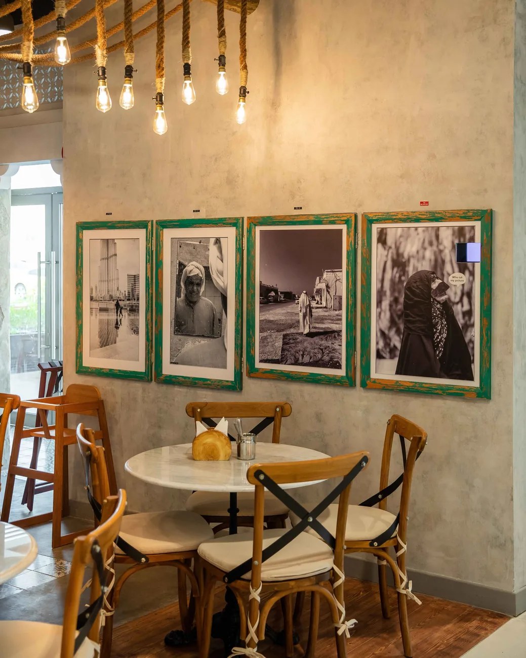 A dining corner at Al Fanar: round tables under hanging bulbs, and framed black-and-white photographs on the wall